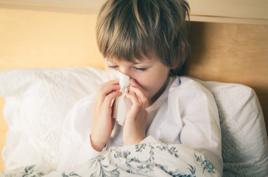 boy is blowing his nose on the bed